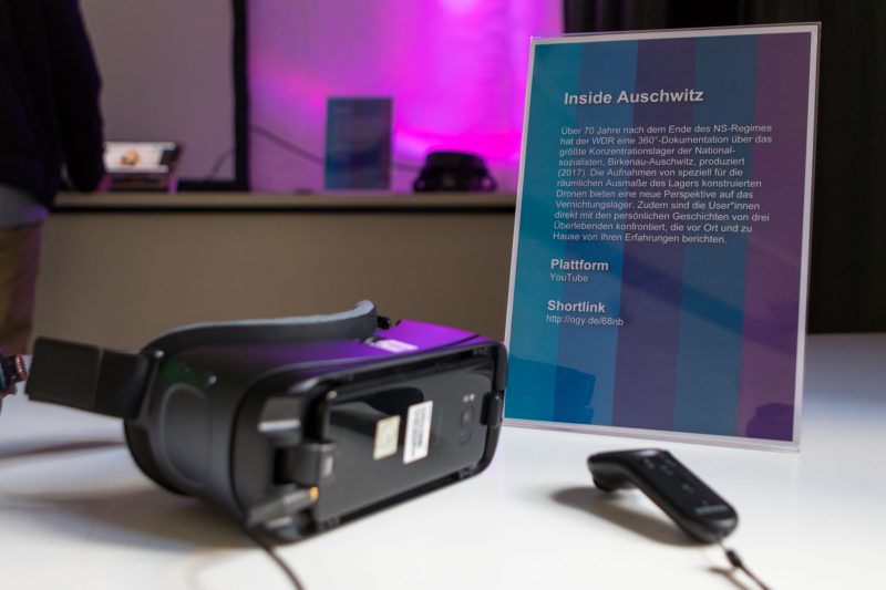 Eine VR-Brille und ein VR-Controller liegen neben einem Aufsteller mit der Beschreibung für das VR-Projekt "Inside Auschwitz"