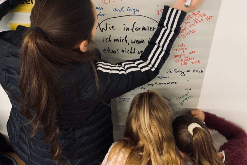 Zwei jugendliche Workshopteilnehmerinnen beschreiben ein Plakat zu der Frage, wie sie sich informieren, wenn sie über ein Thema nicht Bescheid wissen.