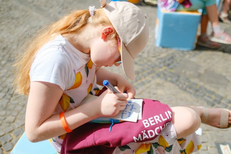 Mädchen mit Sweater vom Berliner Mädchenchor schreibt auf eine Moderationskarte
